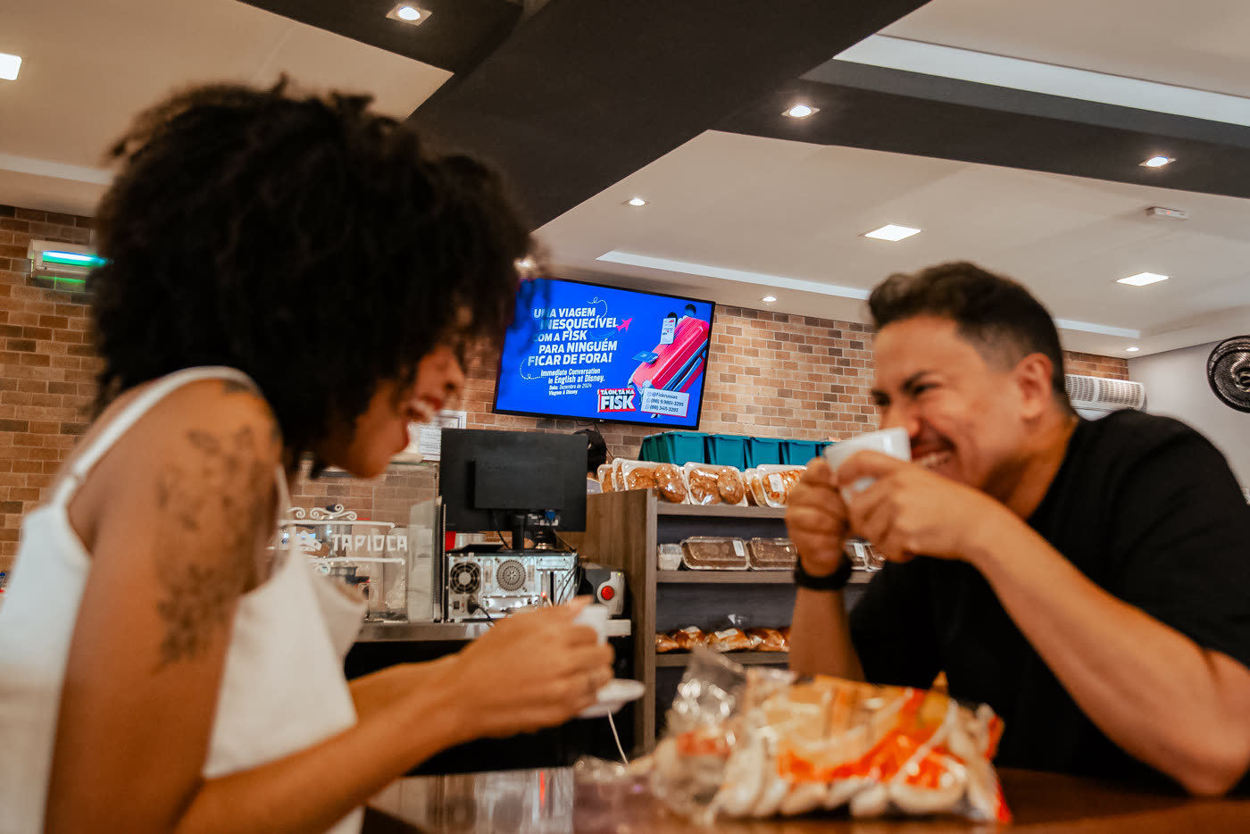 Casal em uma cafeteria com tela ao fundo